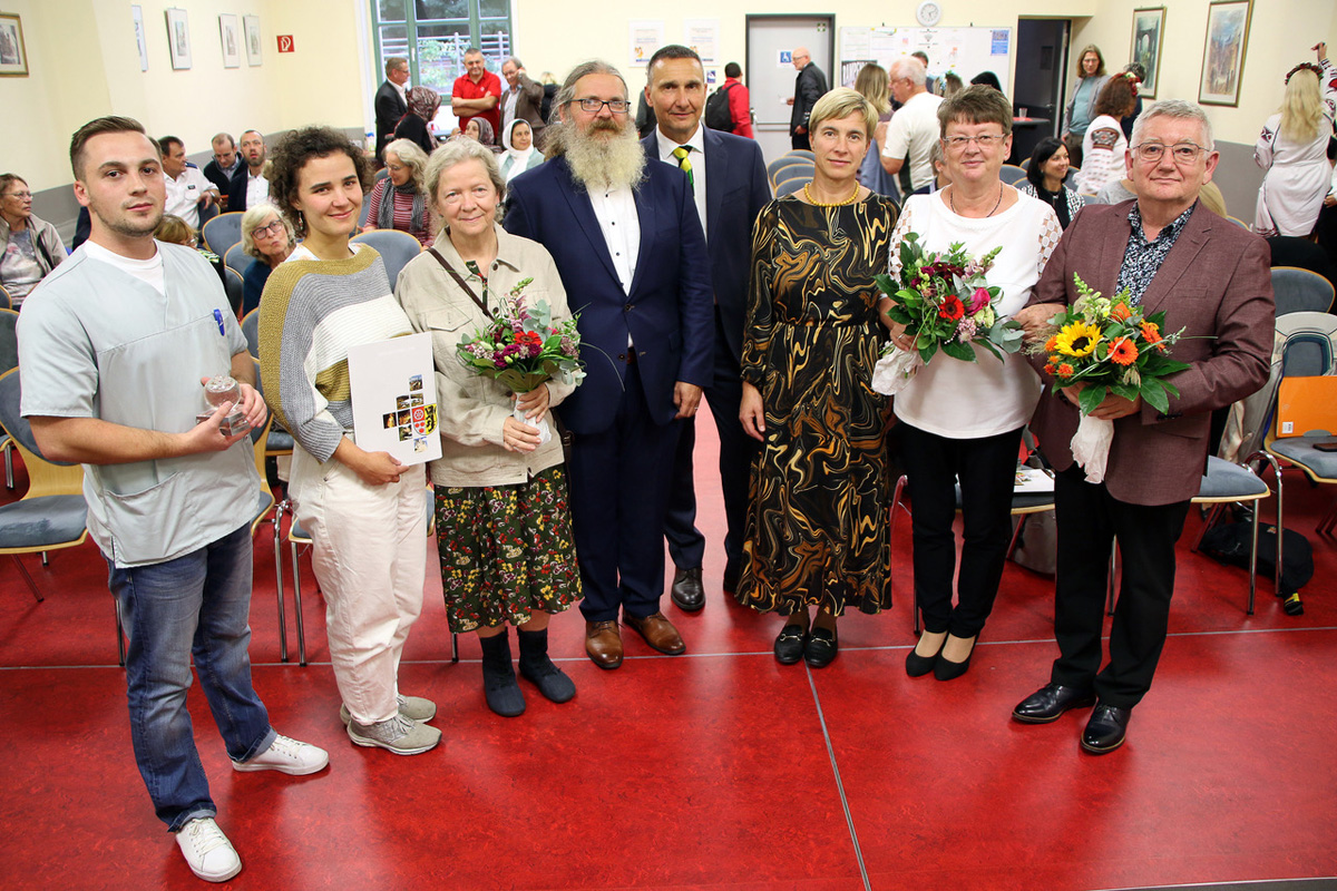 Gruppenaufnahme mit Blumensträußen und einer Urkundenmappe bei der Integrationspreisverleihung 2026 in Apolda